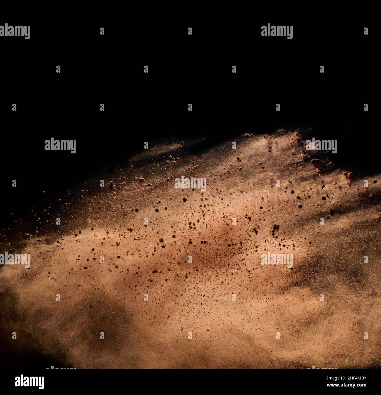 flying brown cocoa particles on a black background. Powder flies up ...