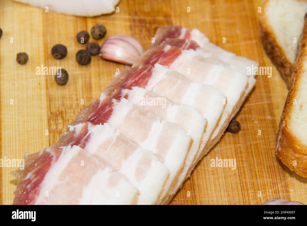 Ukrainian traditional food concept with white bread. Ukrainian raw lard with peppercorn and garlic, knife, slices of salo lying on wooden cutting boar Stock Photo