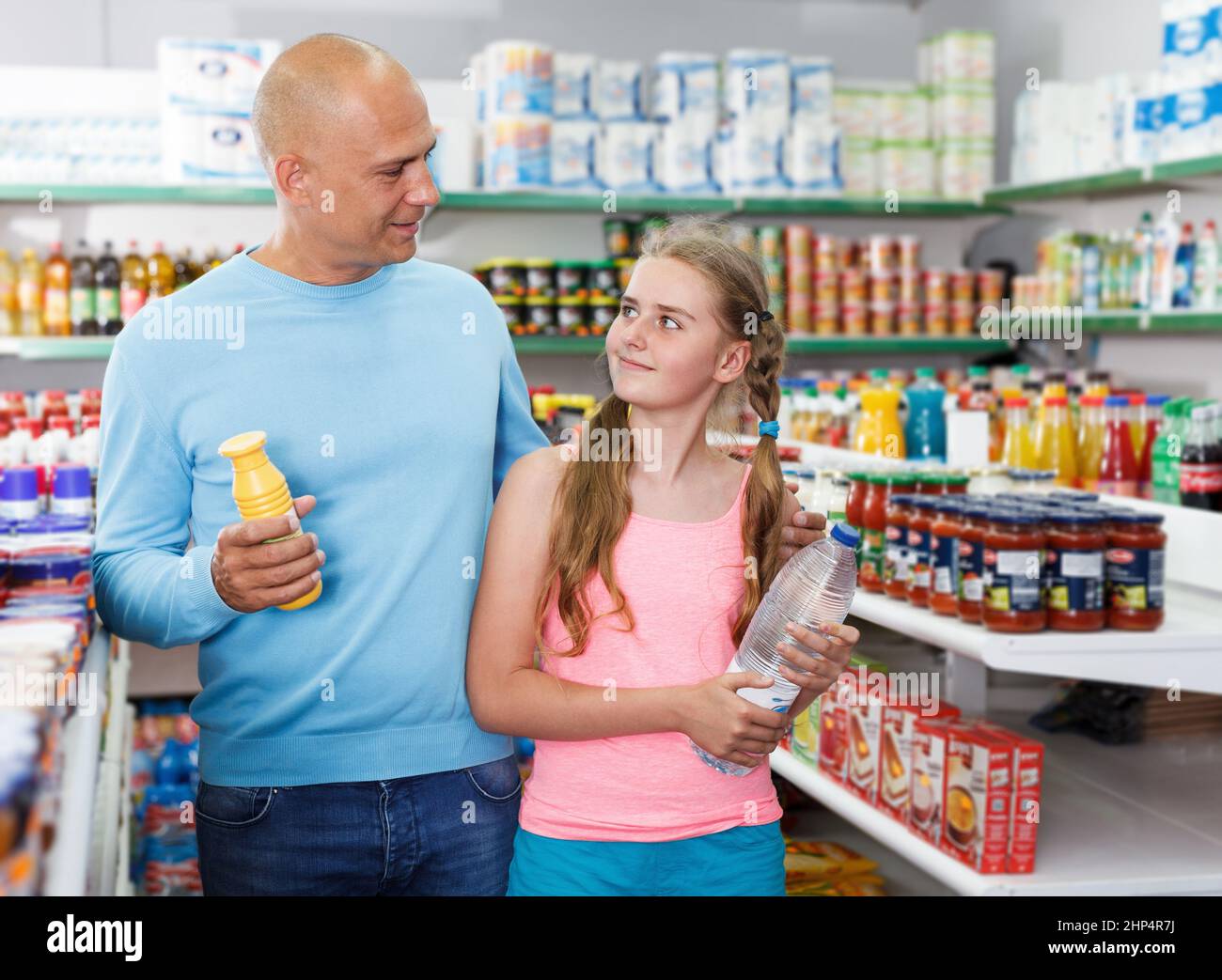 Preteen girl with father holding different goods in supermarket Stock Photo