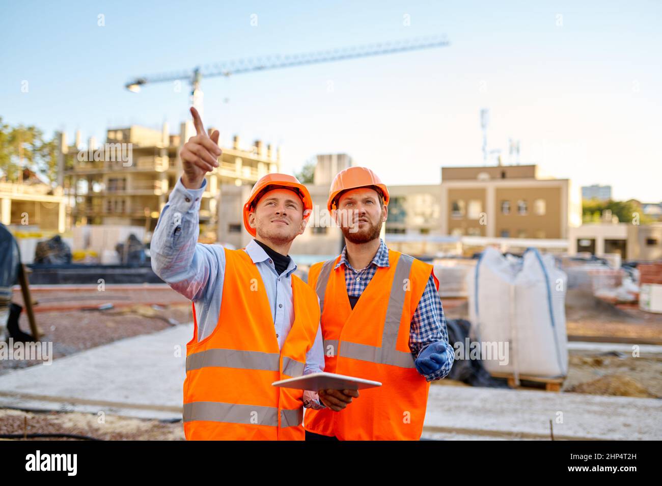 Worker reporting to contractor about execution of building plan using tablet at construction site Stock Photo