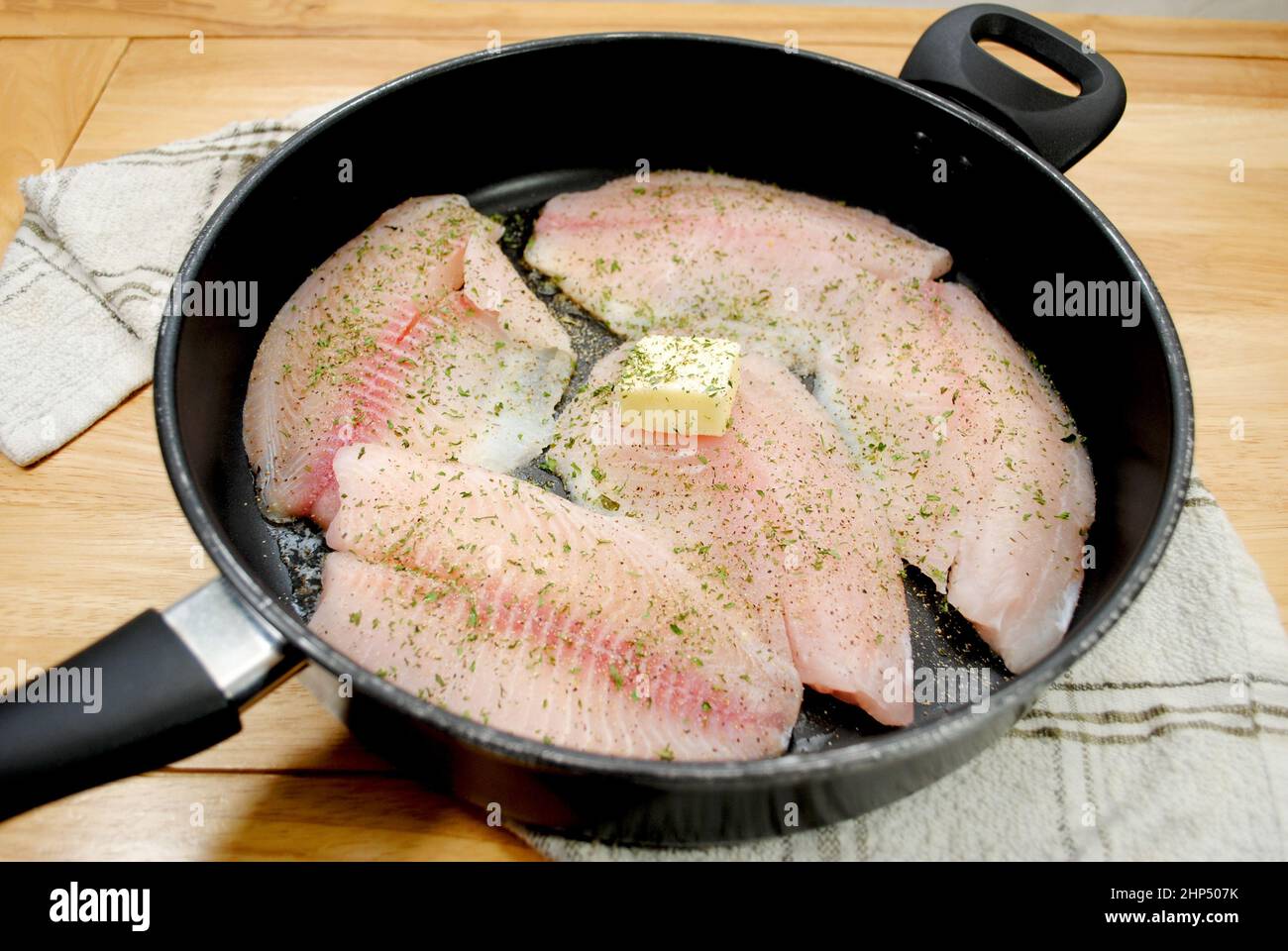 Fresh Tilapia Frying in a Black Pan with Butter and Herbs Stock Photo