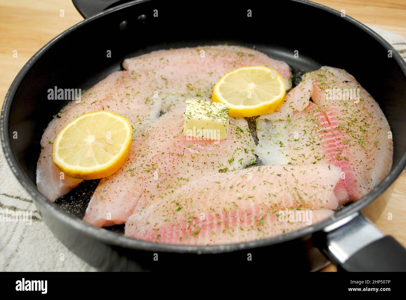 Fresh Tilapia Frying in a Black Pan with Butter, Lemon and Herbs Stock Photo