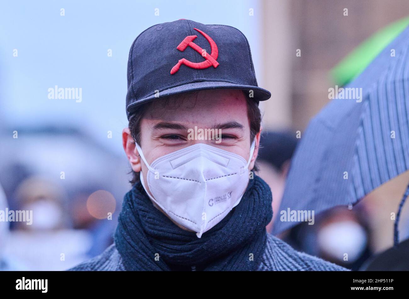 Berlin, Germany. 18th Feb, 2022. Hammer and sickle, a symbol of Marxism-Leninism, is worn by a demonstrator on his cap. A rally of the Berlin peace groups (FRIKO) for a peaceful solution of the conflict between Russia and Ukraine takes place at the Brandenburg Gate. Credit: Annette Riedl/dpa/Alamy Live News Stock Photo