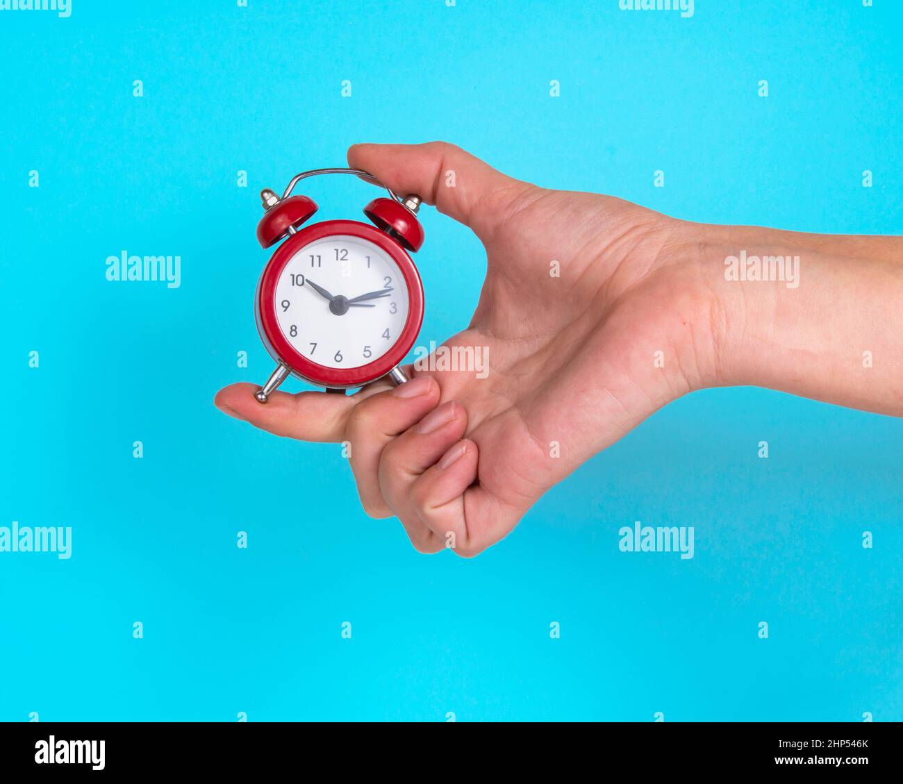 Alarm clock red color in woman hand on bright blue background Stock