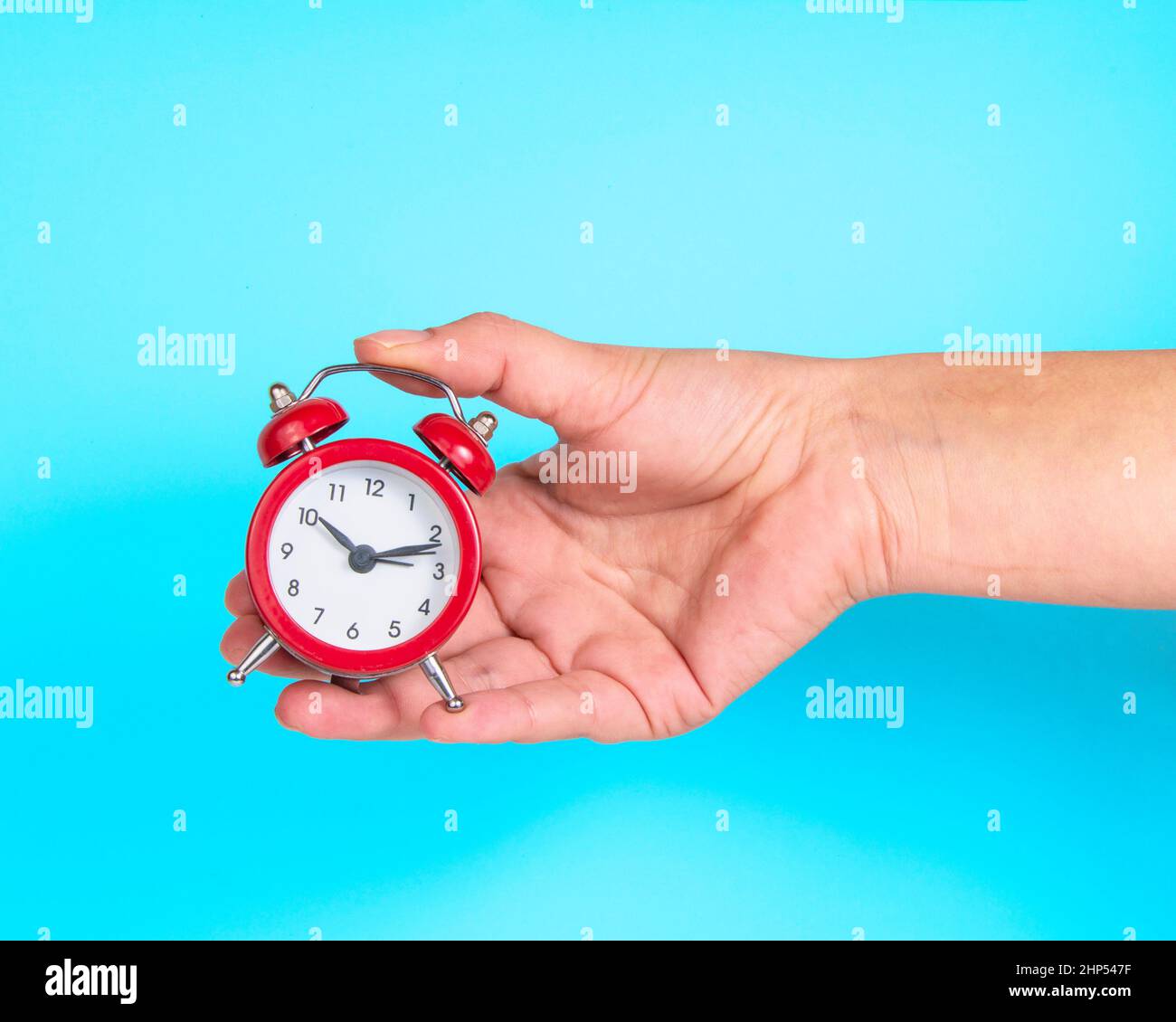 Alarm clock red color in woman hand on bright blue background Stock