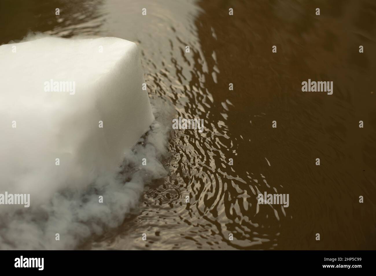 Dry ice evaporates in water. Smoke from chemical reaction. White material bubbles in puddle