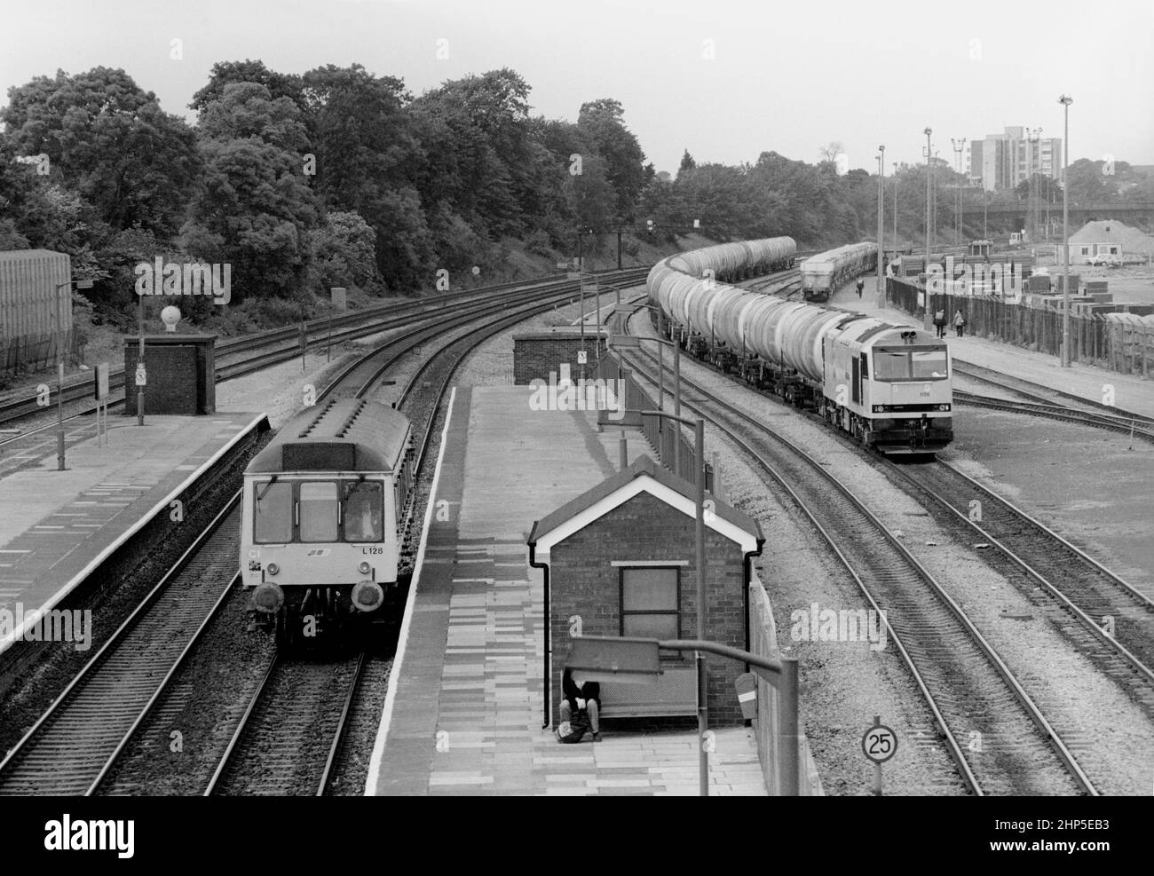 A Class 121 diesel multiple unit number L128 forming a Network SouthEast service pauses at Acton Main Line while class 60 diesel locomotive number 60056 working a train of bogie oil tanks awaits a path north in Acton yard. 10th June 1991. Stock Photo