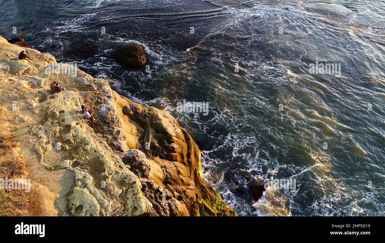 Aerial view of people watching golden sunset at Sunset Cliffs Natural Park while waves crash on rocks, San Diego, California, USA Stock Photo