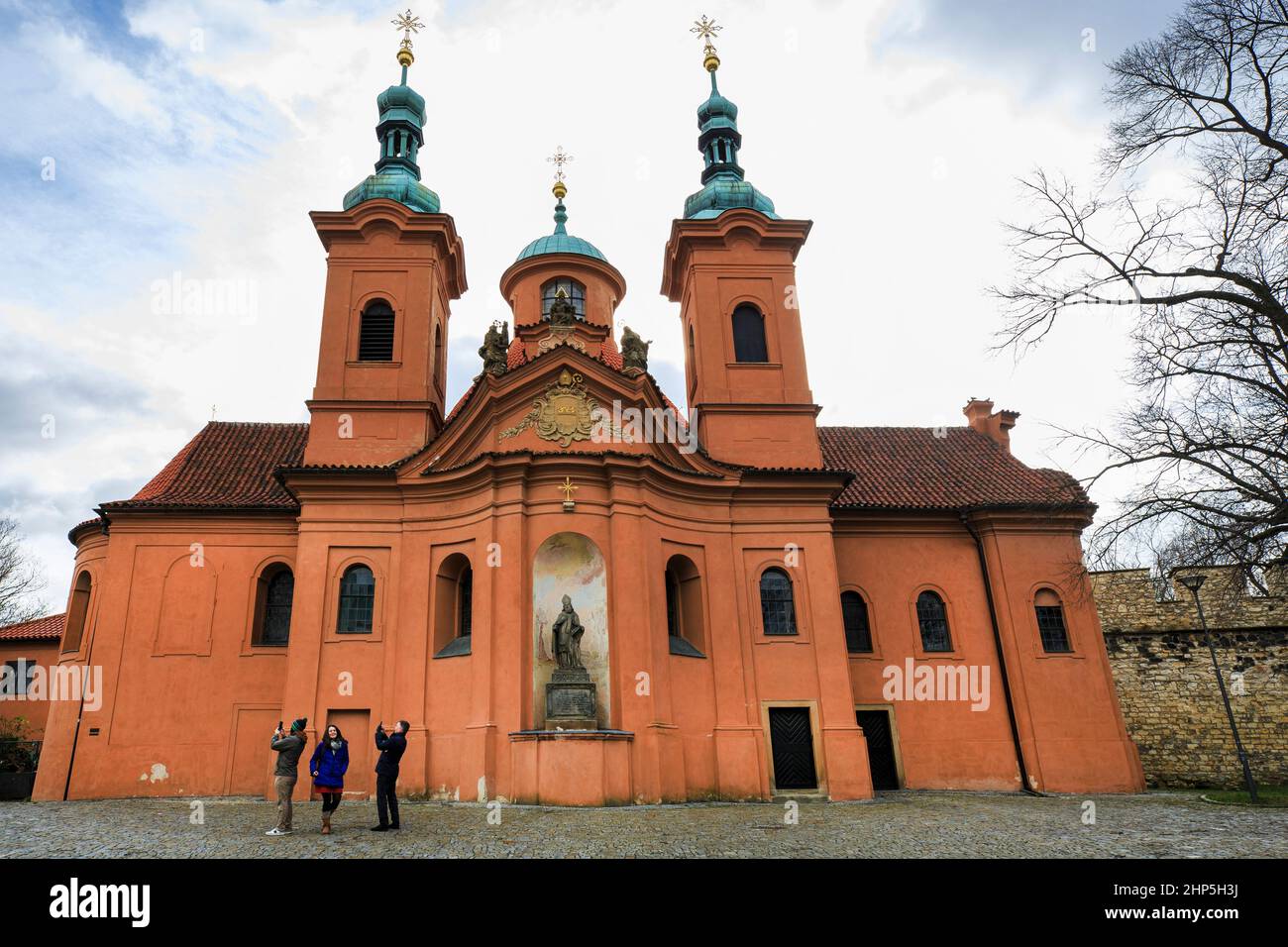 Tourists taking photographs of Church of Saint Vavrinec or St Lawrence with orange facade and twin green cupolas, Petrin Hill, Prague Czech republic Stock Photo