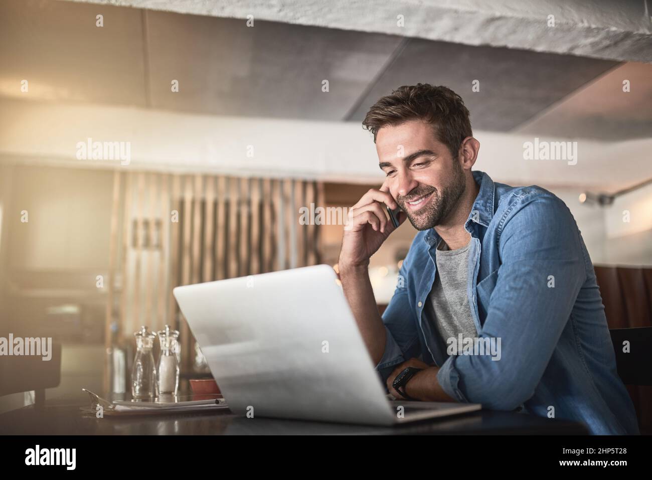 The perfect place for some productivity. Shot of a handsome young man using a laptop and phone in a coffee shop. Stock Photo