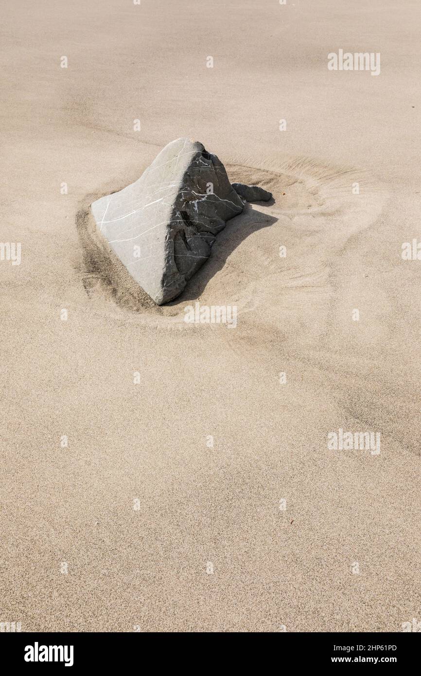 A rock exposed above a sandy beach after tides have receded. Stock Photo