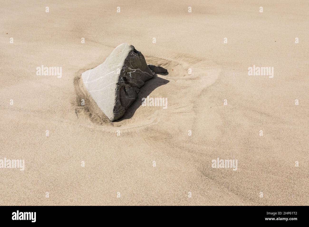 A rock exposed above a sandy beach after tides have receded. Stock Photo