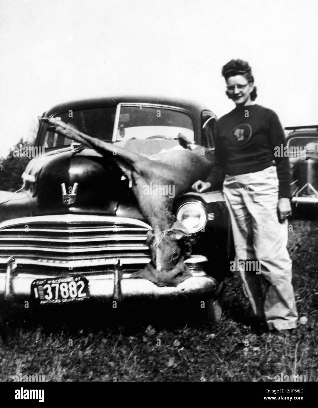 A Wisconsin woman show off her deer strapped to the hood of her car, ca. 1950. Stock Photo