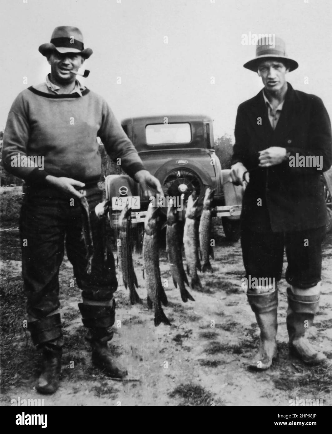 Two successful fishermen show off their northern pike catch in front of their period car, ca. 1925. Stock Photo