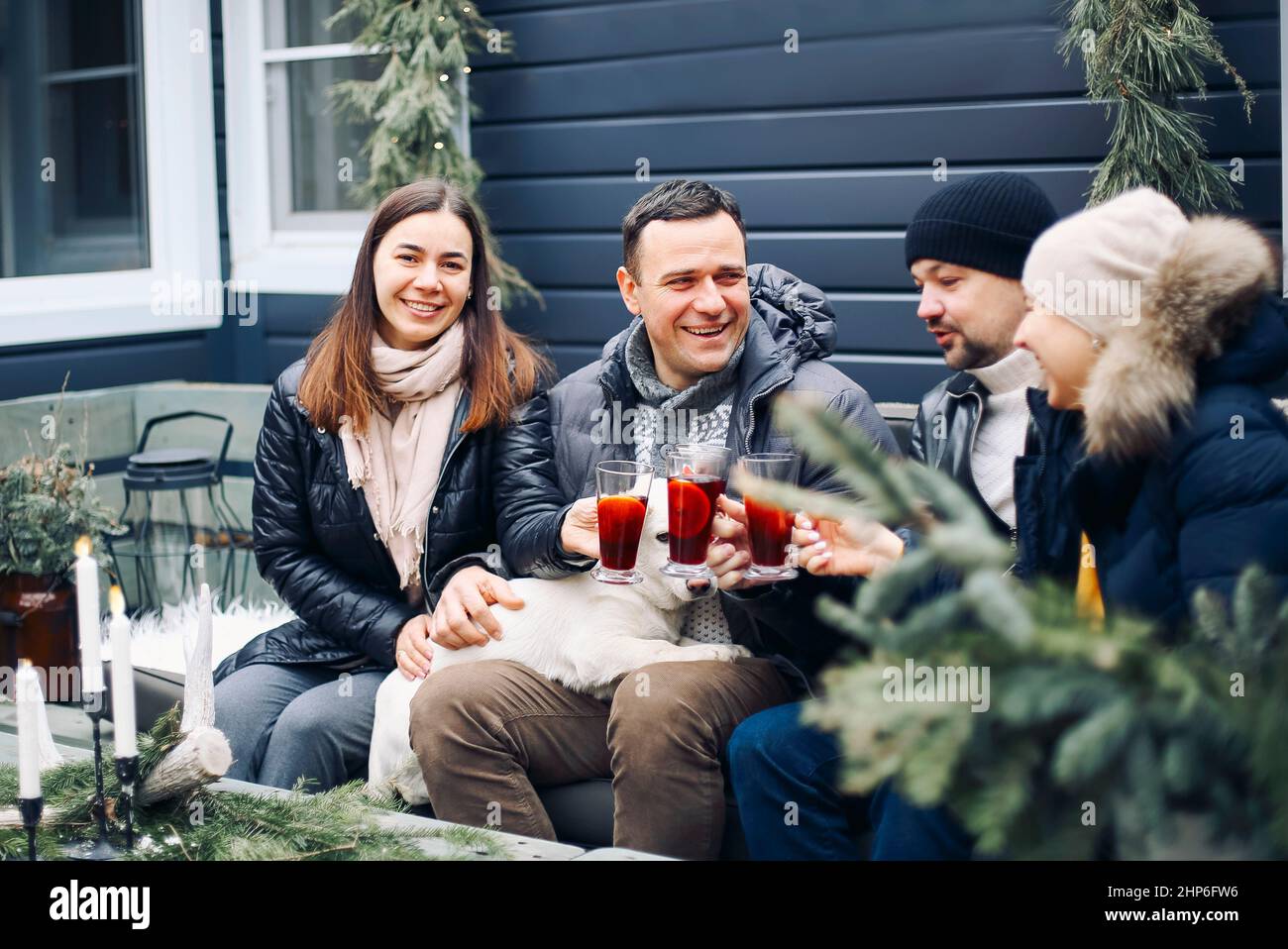 Bonfire party. Joyful young family couple gathering with friends around campfire in winter, happy people preparing and drinking hot mulled wine while Stock Photo