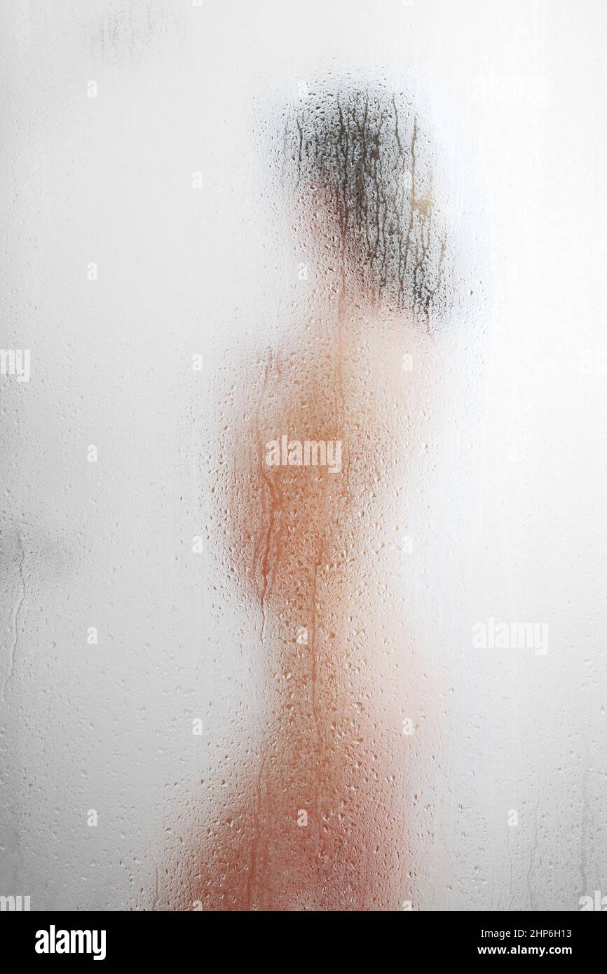 A woman takes a shower through fogged glass with water drops neutral background Stock Photo