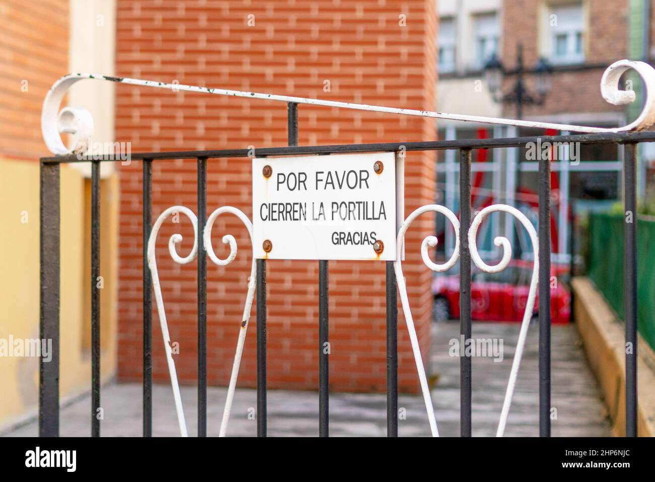 A metal sign on the gate with an ornate iron pattern at the entrance courtyard, with an inscription in Spanish: Please close the gate, thank you Stock Photo