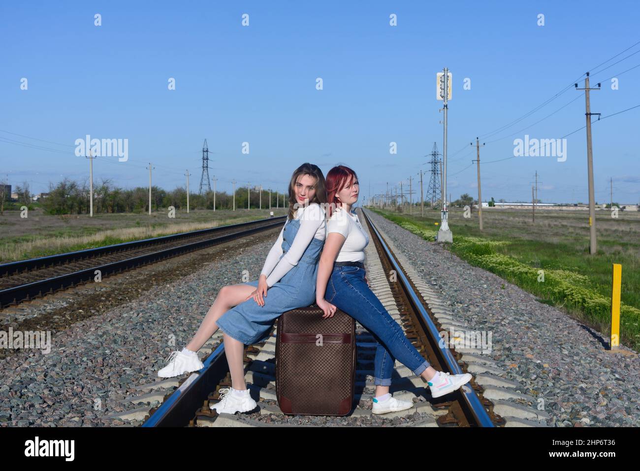 Beautiful young ladies are sitting on large suitcase on the railroad tracks. Travel concept. Stock Photo