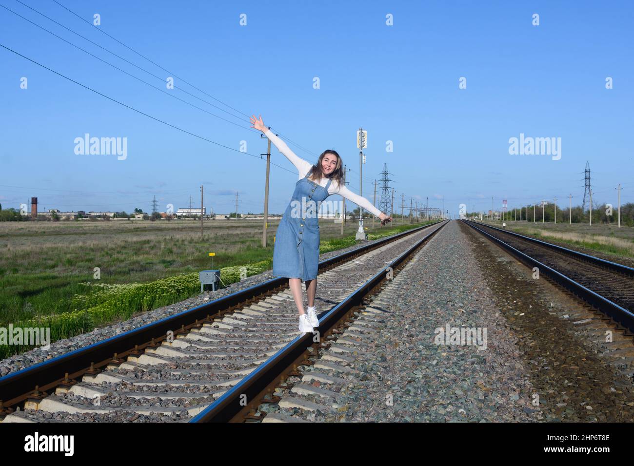 Happy young woman walks on railroad tracks. Keeps arms in balance. Stock Photo