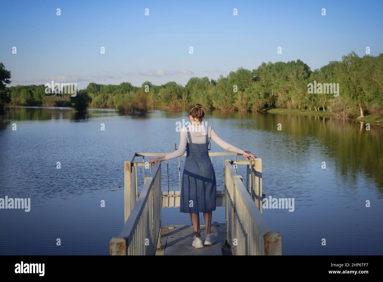 Young woman stands on edge of the bridge looking at water river. View from back. Problem and suicide concept. Stock Photo
