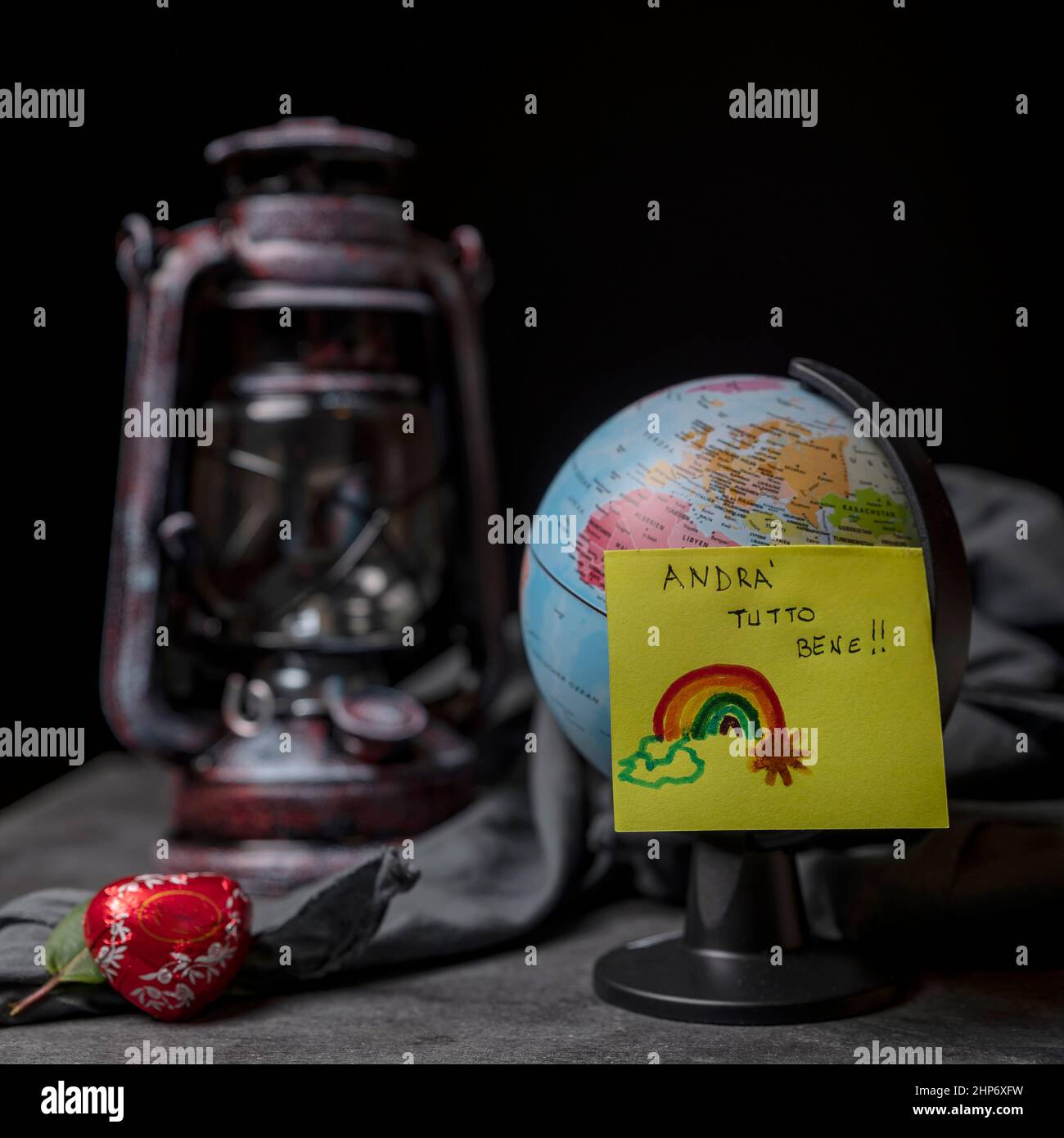 A post it that says 'everything will be fine' in Italian, attached to a small globe with a vintage lantern in the background Stock Photo