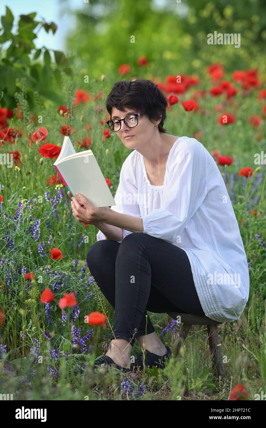 Woman In A Poppy Field Reading and Holding A Book Stock Photo