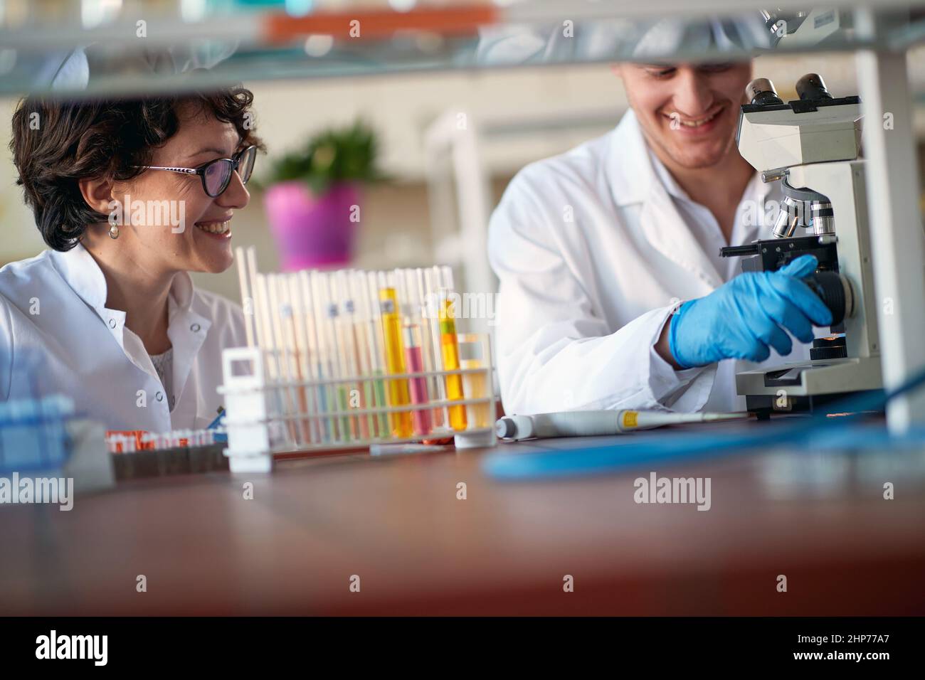 Young chemistry university colleagues enjoying working with a microscope in a laboratory in a relaxed atmosphere. Science, chemistry, lab, people Stock Photo