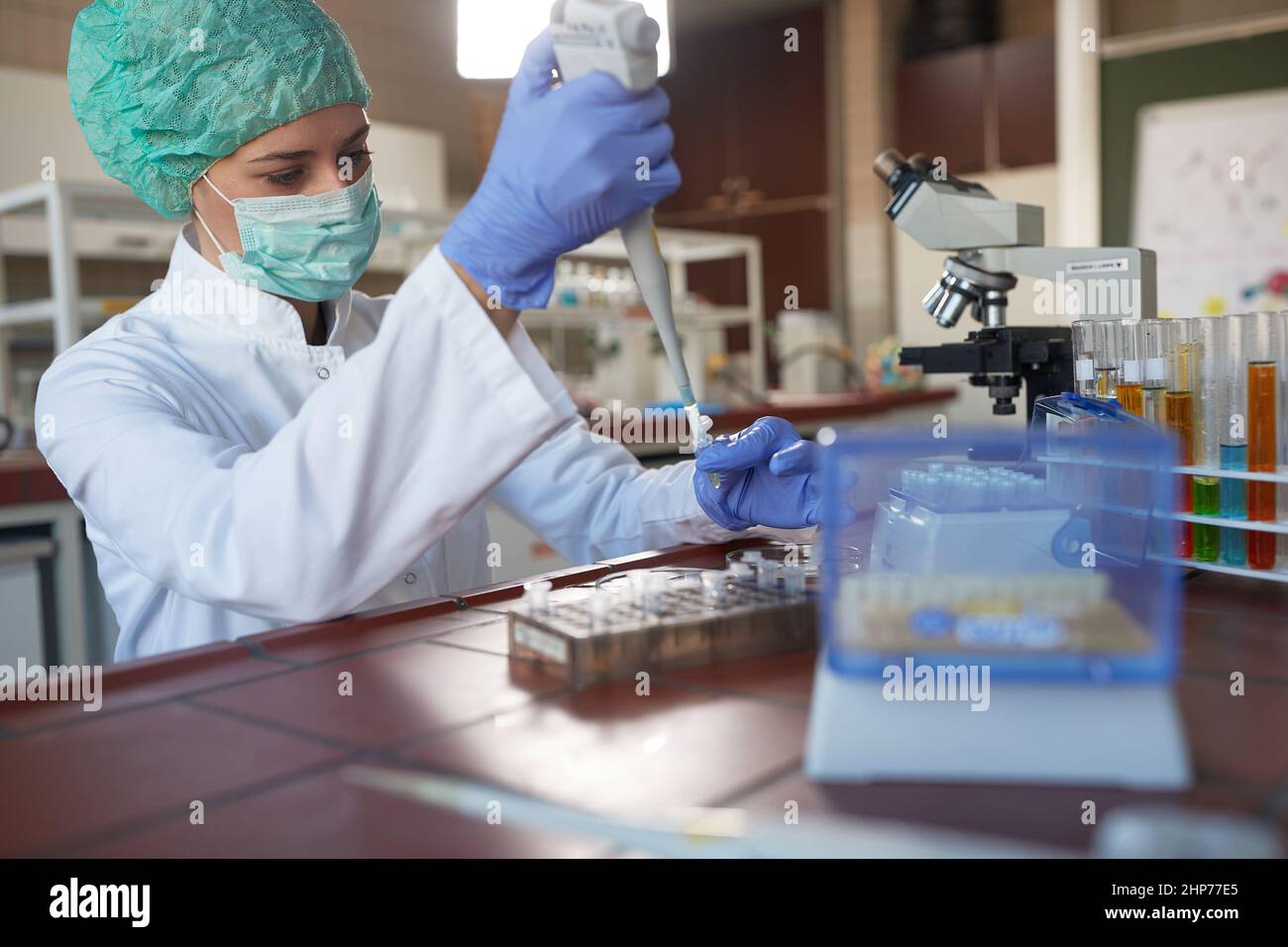 A young female scientist in protective gear taking samples for analysis in a sterile laboratory environment. Science, chemistry, lab, people Stock Photo