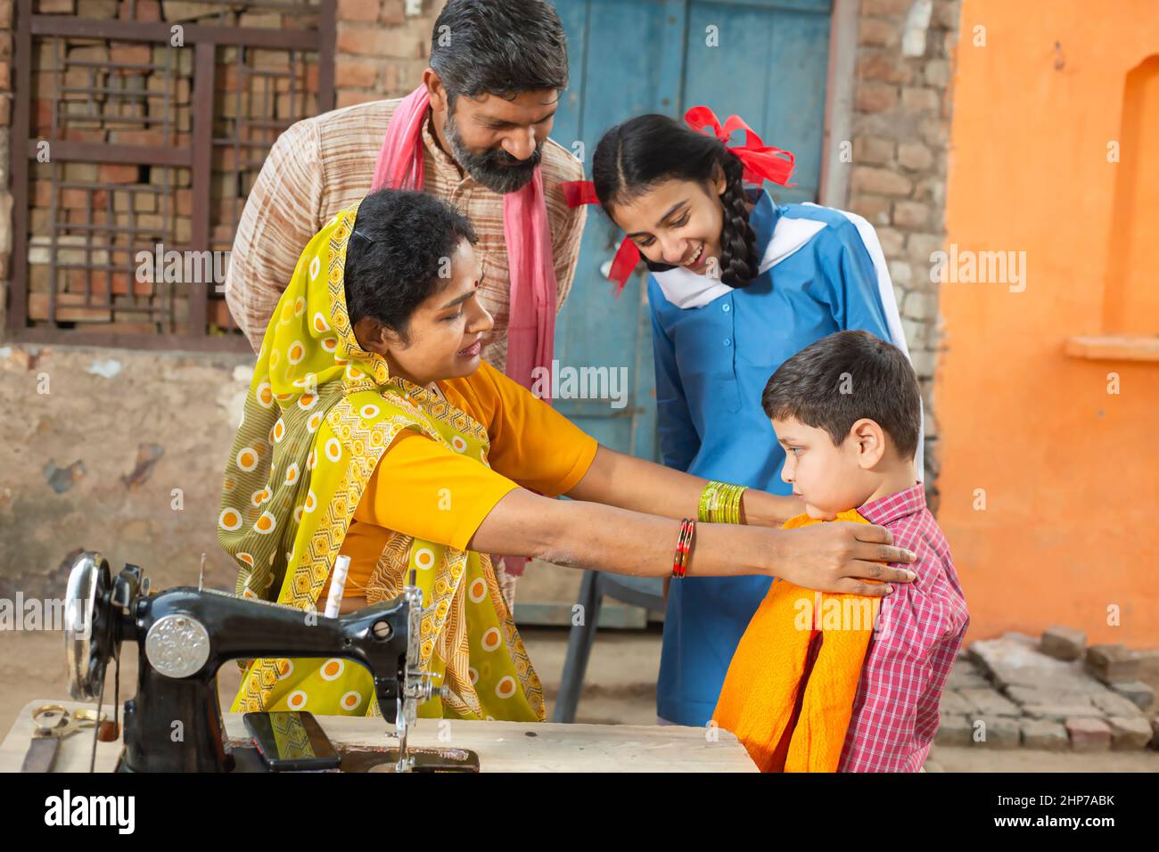Indian mother check cloths size on her son while husband and daughter looks at him, sewing cloths on sewing machine. Small family, lifestyle. Stock Photo
