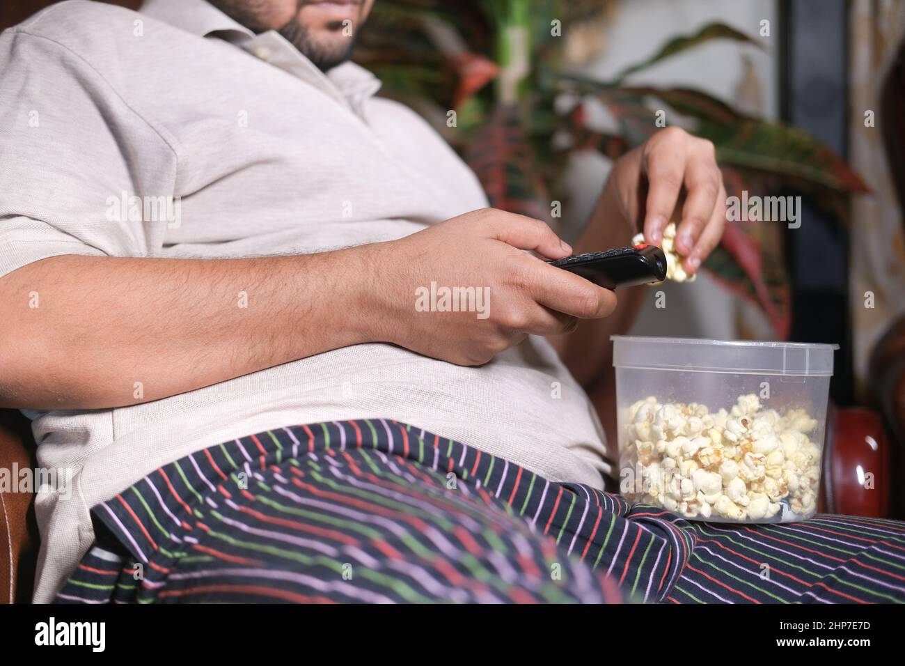 young man eating popcorn and holding popcorn sitting on sofa  Stock Photo