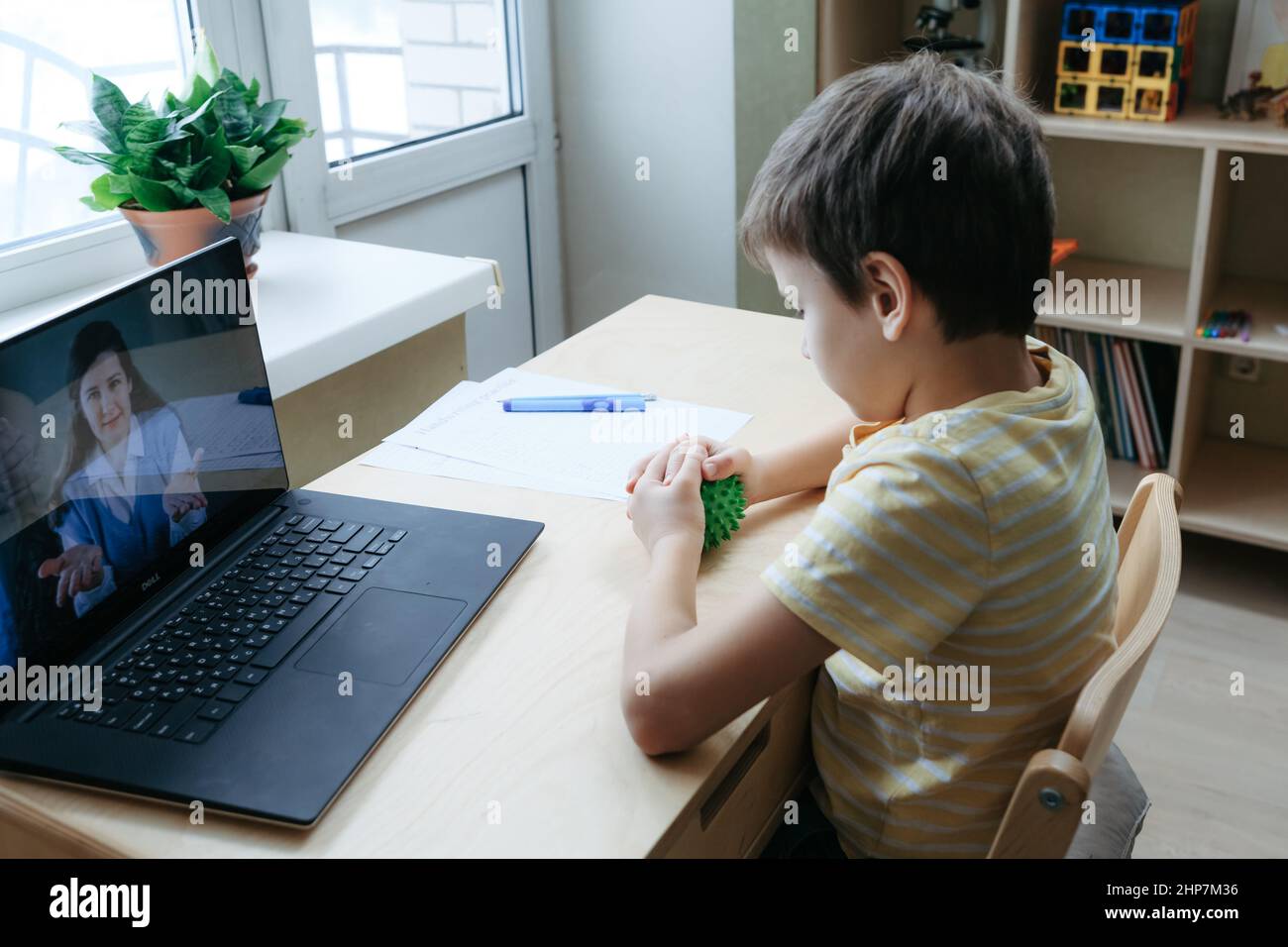 8 years old boy sit by desk with laptop and do exercise with massage ball Stock Photo