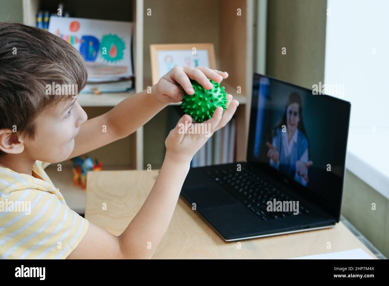 8 years old boy sit by desk with laptop and do exercise with massage ball Stock Photo