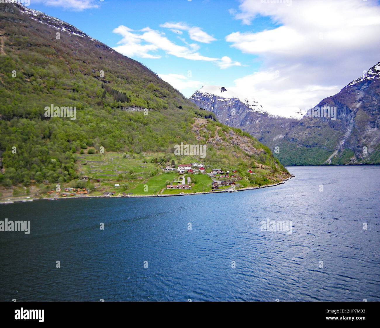 The little village perched on the steep fjord bank with the snow capped mountains behind Stock Photo