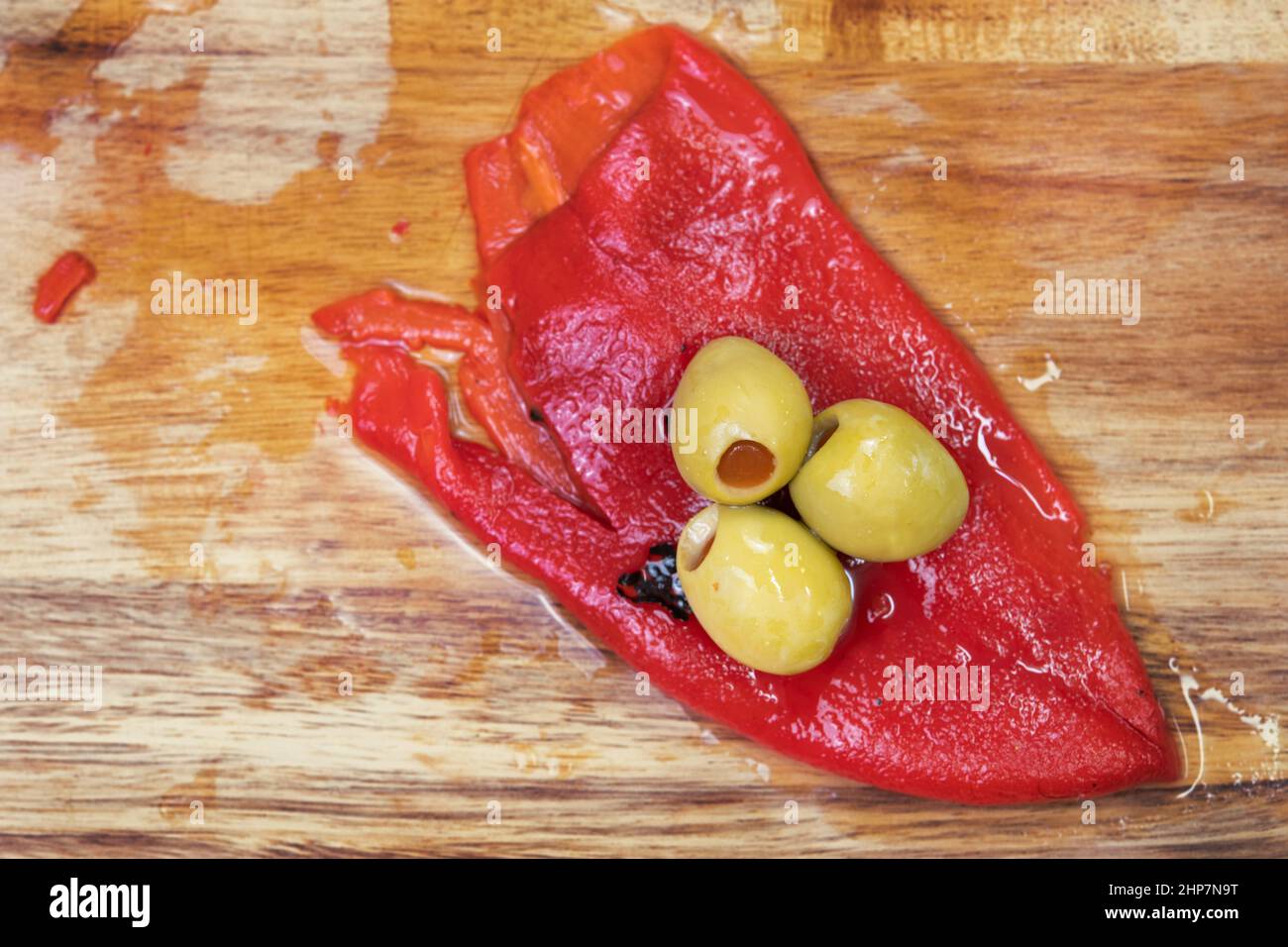 Green stuffed olives and red bell pepper in cutting board. Stock Photo