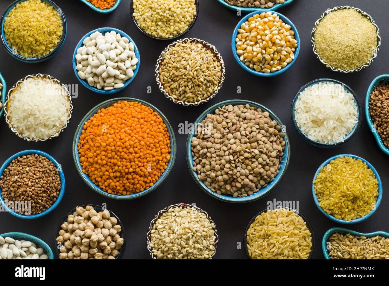 Uncooked dry cereal food group in ceramic bowls on black surface.Top