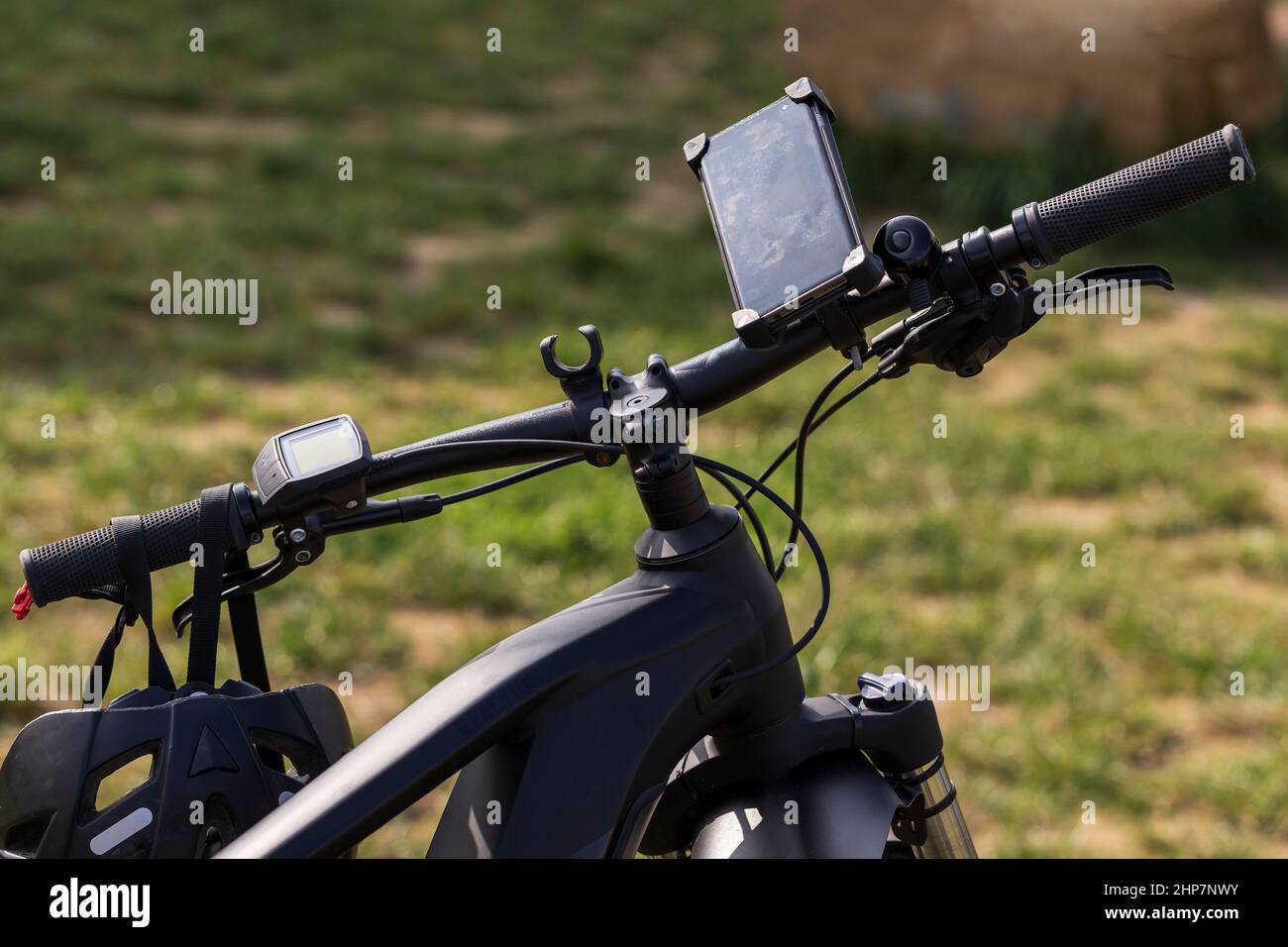 Electric bicycle handlebars. A navigation computer is attached to the handlebars and a bicycle helmet hangs on them. Stock Photo