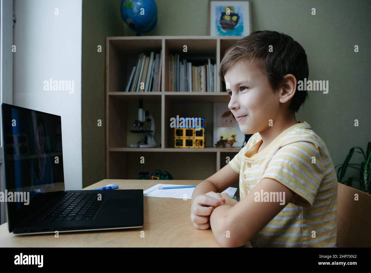 8 years old boy sit by desk with laptop and do writing task during