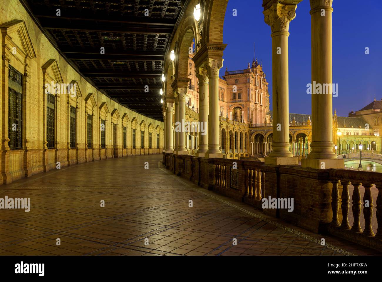 Spanish Square - Wide-angle dusk view of illuminated ground-level portico curving along semi-circular brick building at Spanish Square, Seville, Spain. Stock Photo