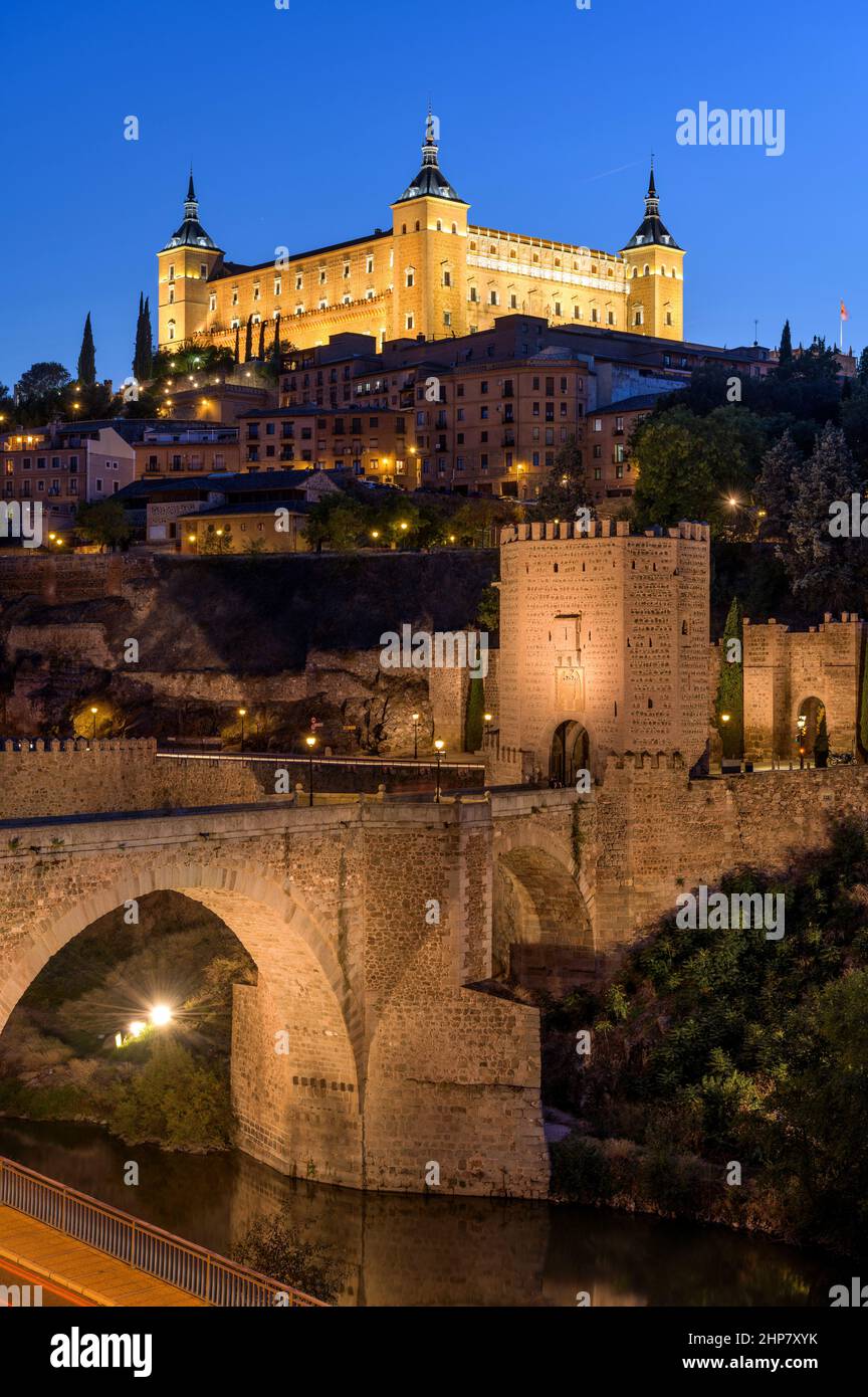 Toledo at Dusk - Vertical dusk view of historic city Toledo at Puente de Alcántara, with Alcázar fortress standing tall at top of hill. Toledo, Spain. Stock Photo