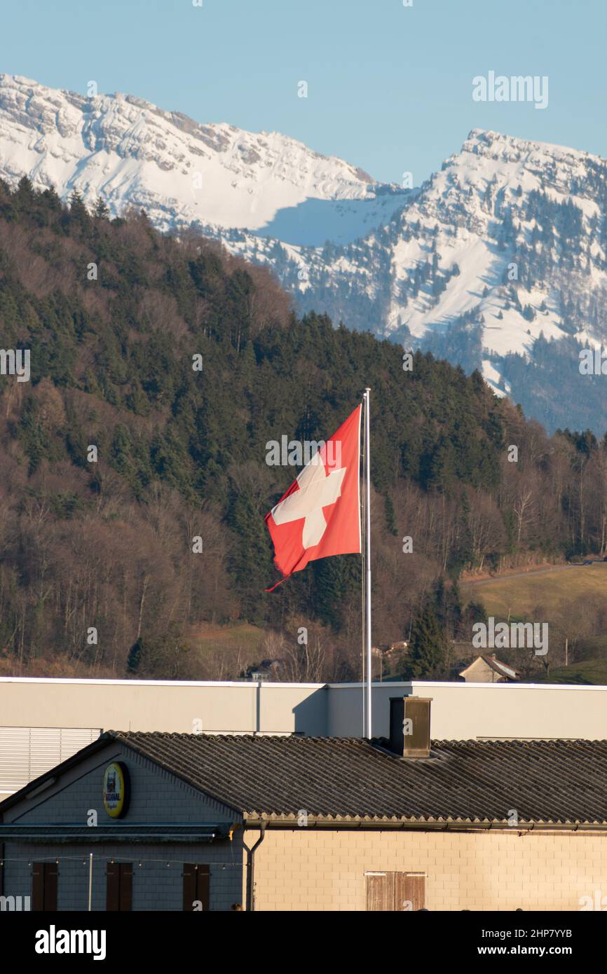 Wangen-Lachen, Switzerland, February 13, 2022 Waving swiss flag with the snow covered alps in the background Stock Photo