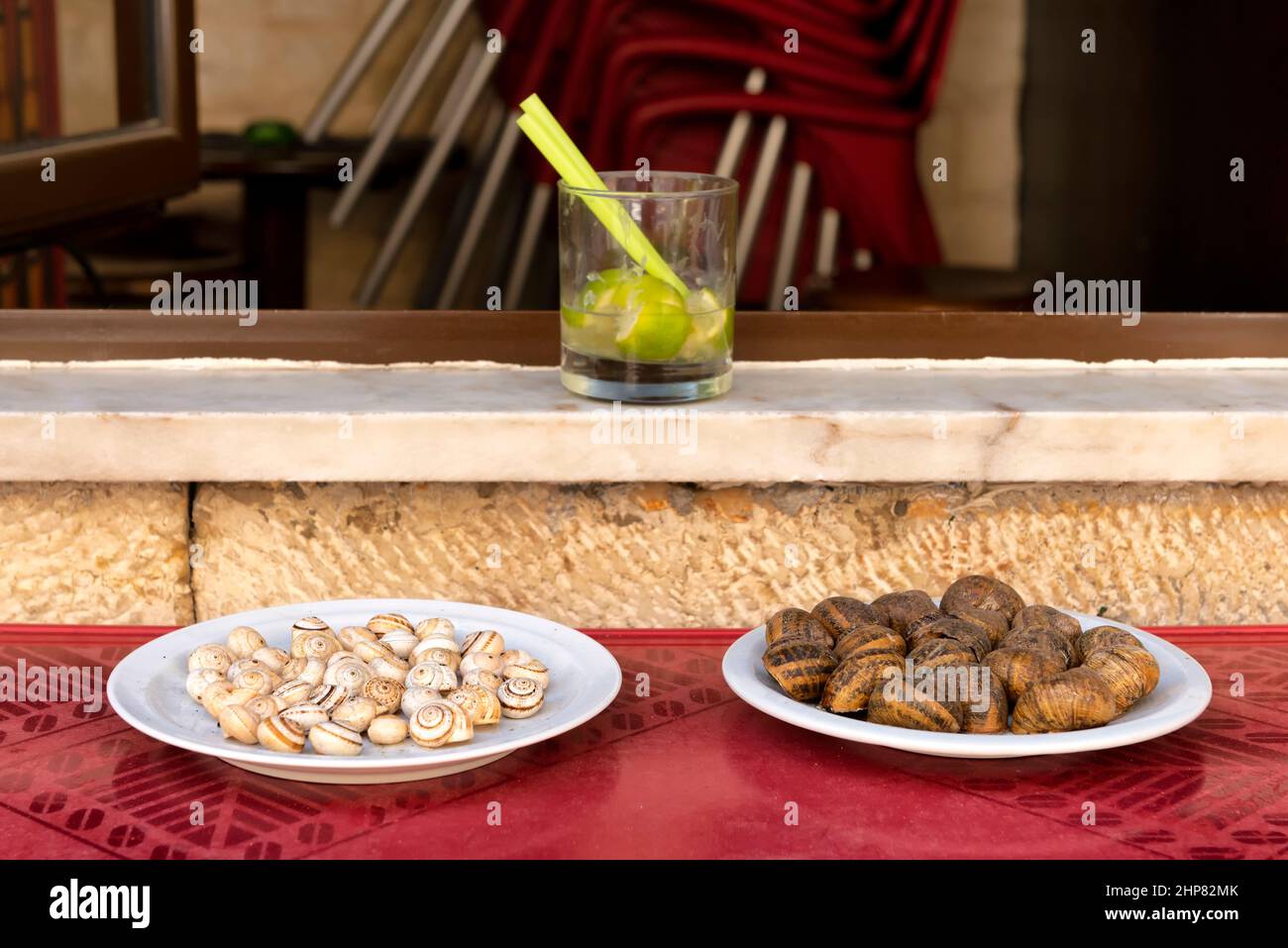 Two plates with different snails and a glass of caipirinha Stock Photo