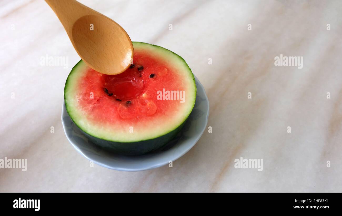 Wooden spoon trying to dig into a small watermelon cut in half. With copy space on the right. Stock Photo