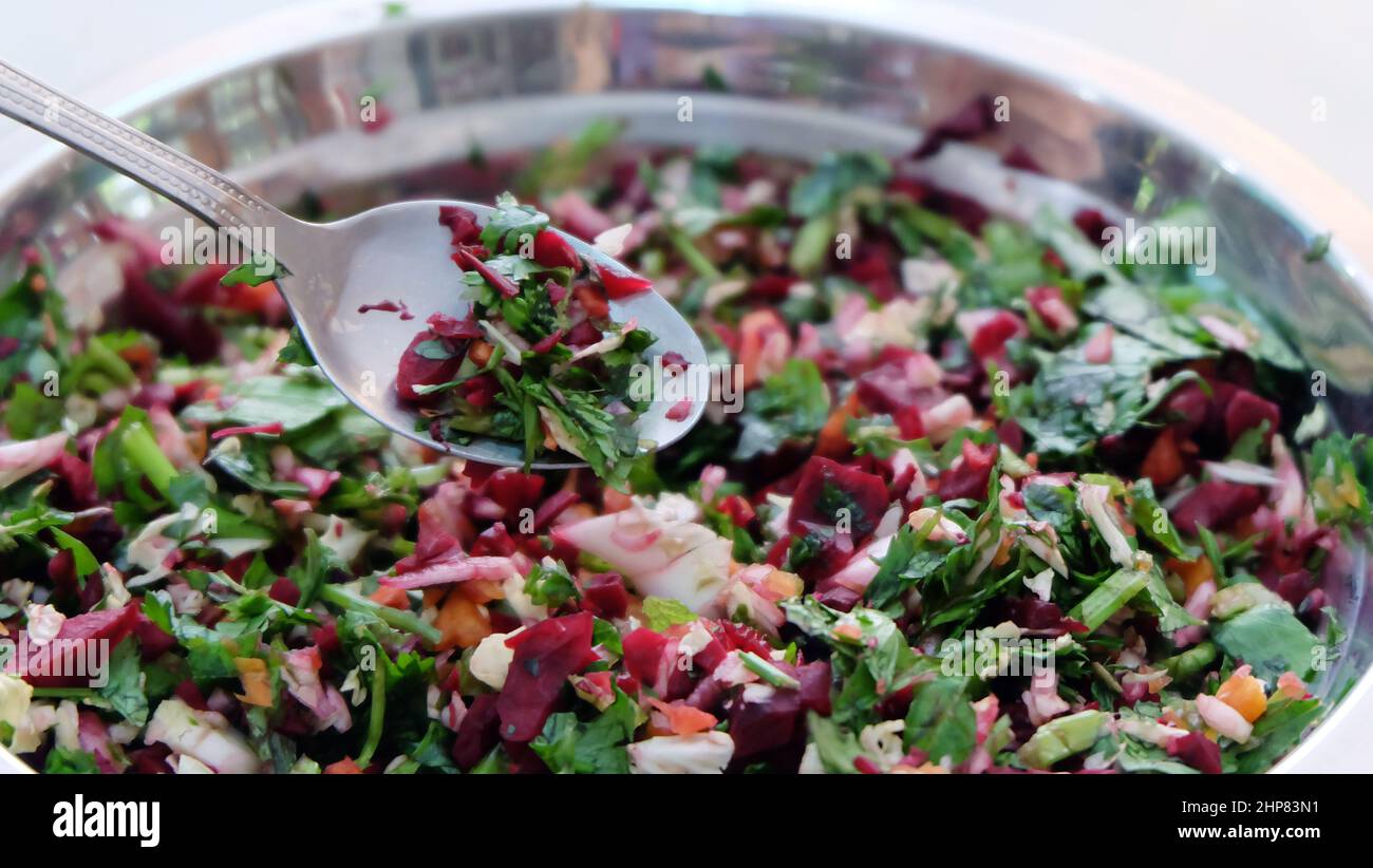 A bowl of fresh and raw vegetable chop, with coriander leaves, pak choy, carrot and beetroot. With a metal spoon scooping out some. Stock Photo