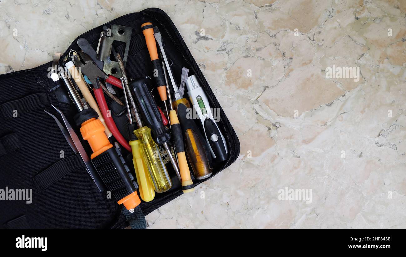 A tool bag with unsorted tools of tweezers, screwdrivers, pliers, and others. Placed on a marble surface with copy space on the right. Stock Photo