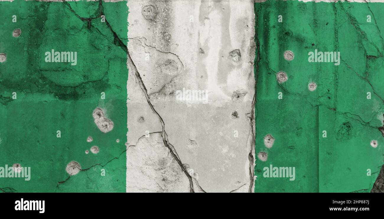 Full frame photo of a weathered flag of Nigeria painted on a cracked concrete wall with bullet holes. Herder–farmer conflicts in Nigeria concept. Stock Photo