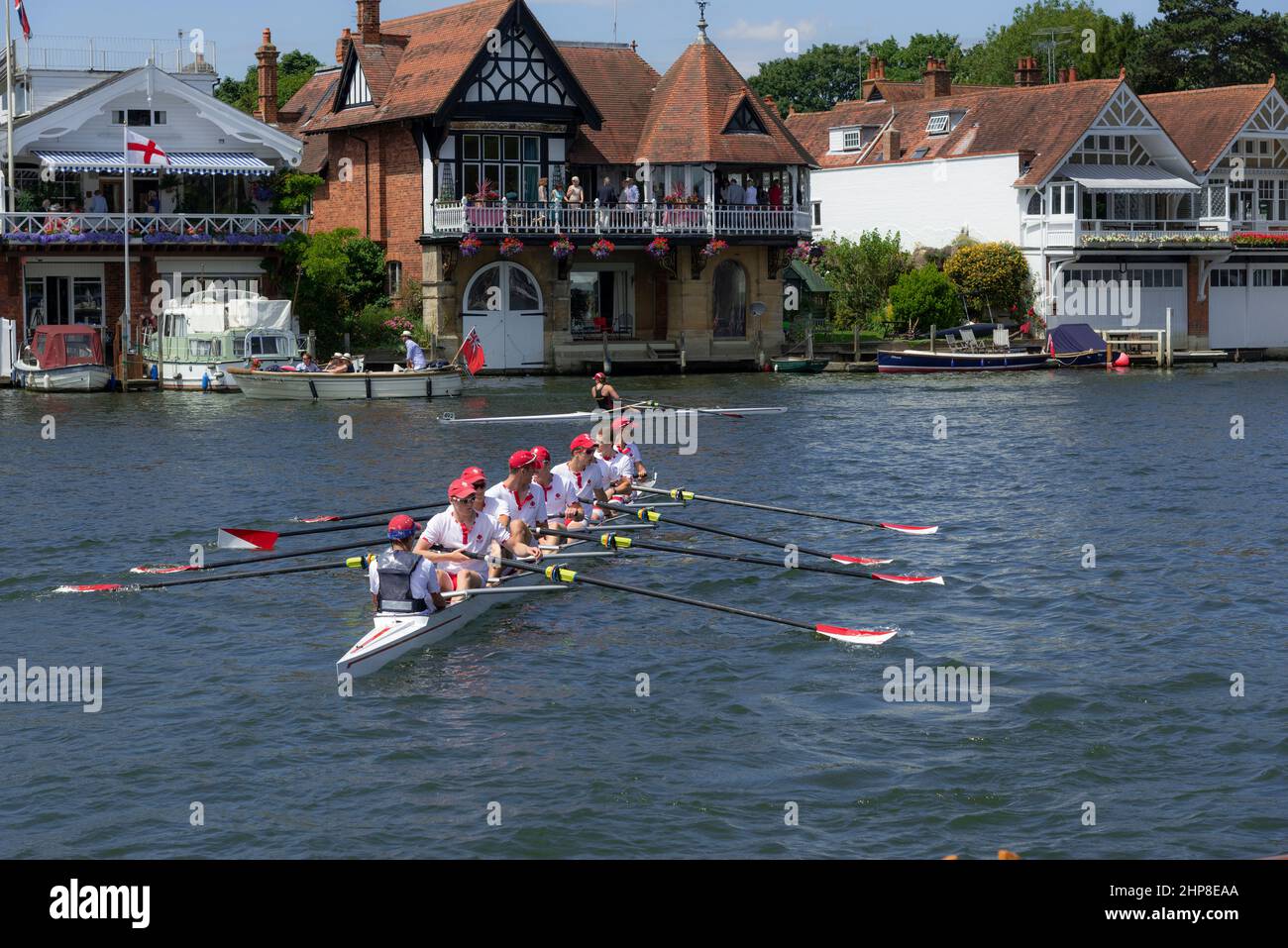 River Thames scene of rowing eight and waterside houses during the Henley Royal Regatta, Henley-on-Thames, Oxfordshire, England, UK Stock Photo
