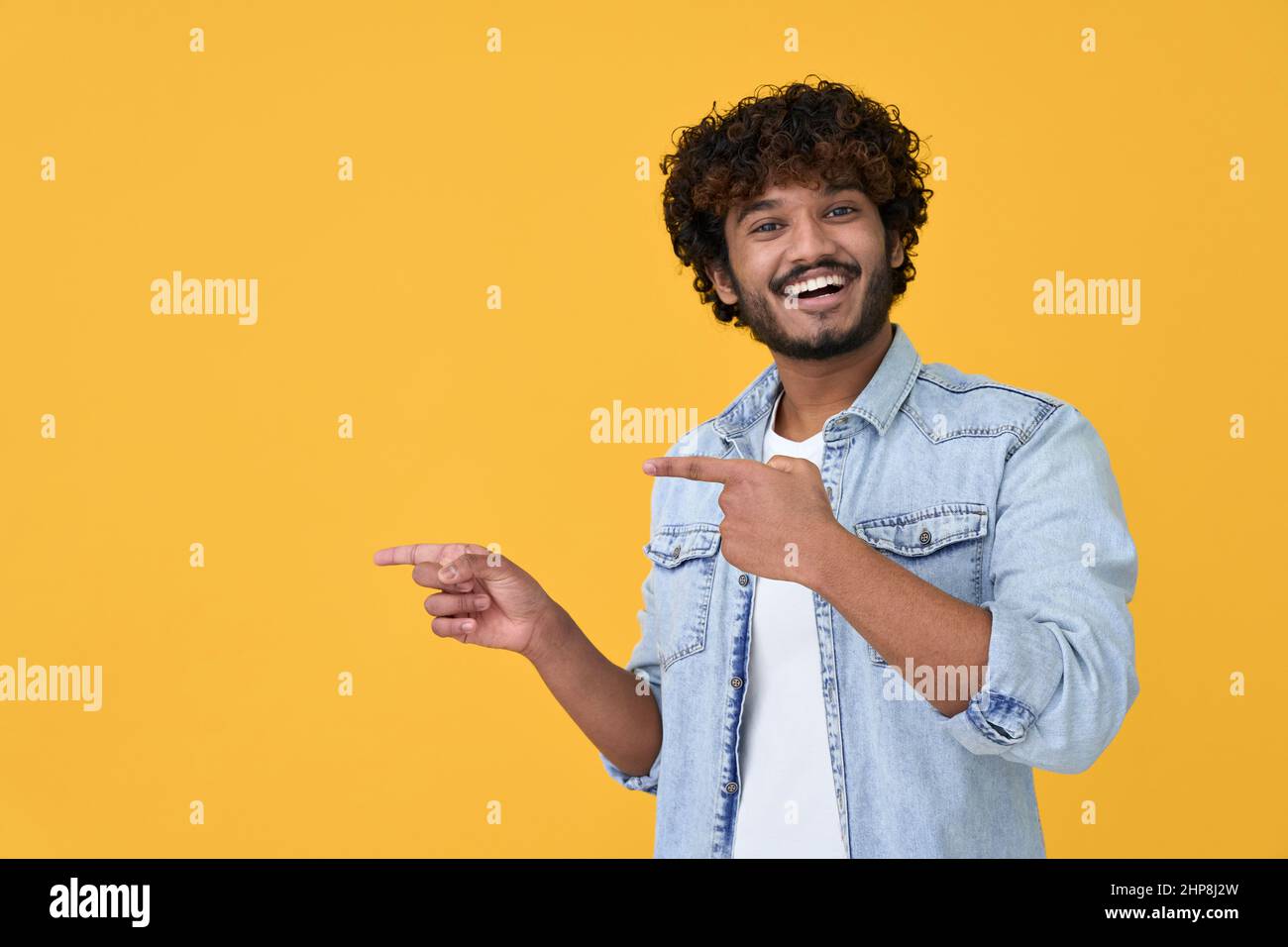 Happy excited young indian man pointing on yellow background. Stock Photo