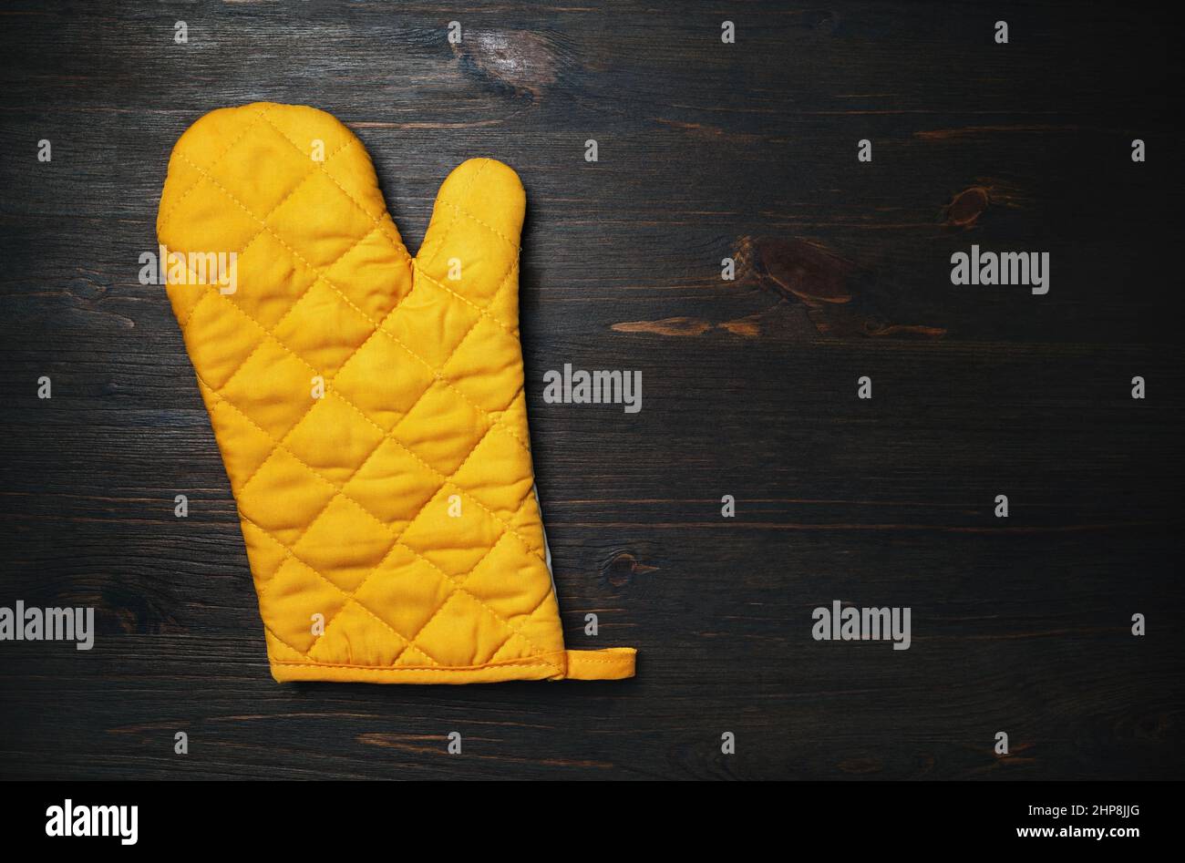 Yellow cooking glove on wood table background. Kitchen utensil. Space for text. Flat lay. Stock Photo