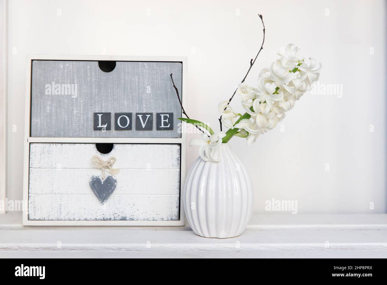 White hyacinth in a vase next to a small chest of drawers with the inscription Love. boho house Stock Photo