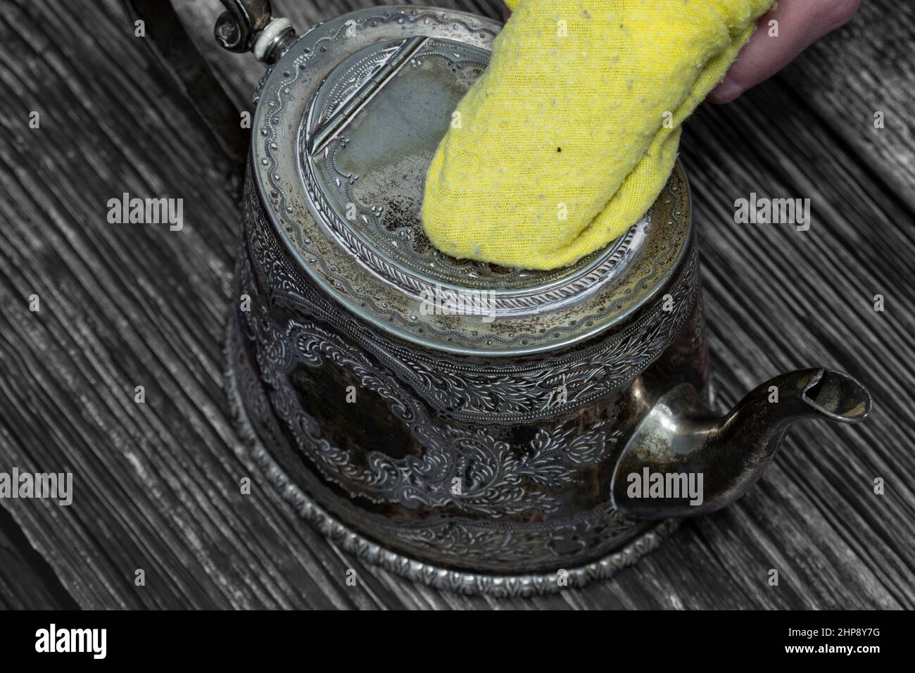 Cleaning antique tarnished silver teapot with a yellow duster. On a wood background Stock Photo